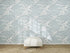 A white ottoman sits on a woven rug in front of a wall covered with Making Waves Wallpaper | Blue. Sunlight creates soft shadows on the floor and wallpaper mural.