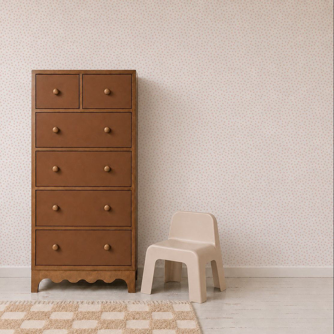 A tall brown wooden dresser with knobs stands next to a small beige plastic chair on a light wooden floor with a rug, against a pale wall adorned with Sprinkle Wallpaper in pink.