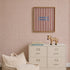 A small dresser with books and a zebra figurine stands against a statement wall featuring the Sprinkle Wallpaper in Cherry Red. Above the dresser, a striped artwork with blue text is displayed. A cream beanbag chair sits in the foreground.