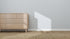 A light wood dresser with round knobs stands against a wall featuring Blue Sprinkle Wallpaper | Sample. Sunlight casts a rectangular shadow, highlighting the textured beige carpeting and showing off the wallpapers color and quality.