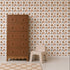 A tall brown dresser stands next to a small beige plastic chair, set against a wall decorated with the Sun and Rainbows Wallpaper. The light wood floor features a tan and white checkered rug partially in view.
