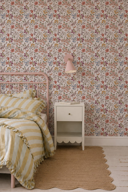 A cozy bedroom features Sunlit Butterfly Meadow Wallpaper, a pink metal bed with yellow and white striped bedding, a small white nightstand, a pink wall lamp, and a tan woven rug on a white wooden floor.