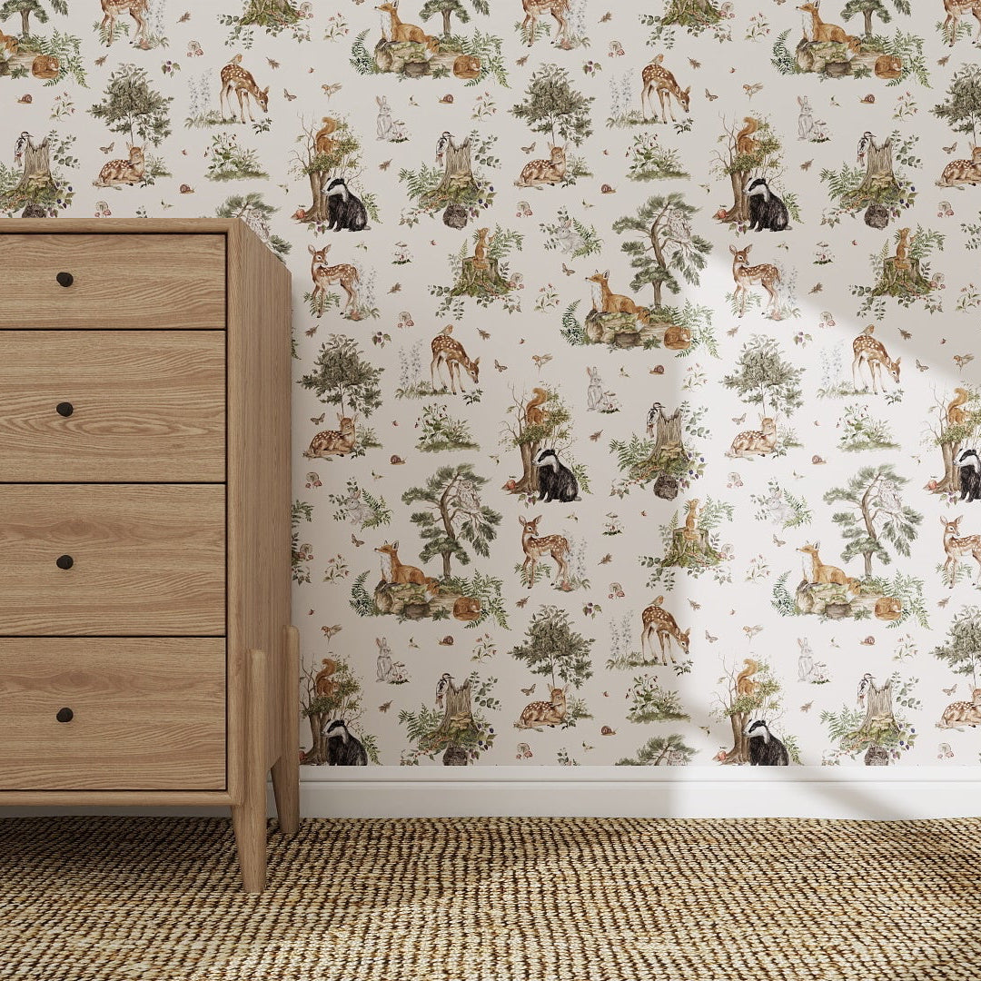 A wooden dresser with three drawers stands on a woven carpet by the wall, featuring the Tales Beneath The Trees Wallpaper Sample, Cream, which highlights its playful animal design and quality in the sunlit room.
