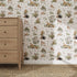A wooden dresser with three drawers stands on a woven carpet by the wall, featuring the Tales Beneath The Trees Wallpaper Sample, Cream, which highlights its playful animal design and quality in the sunlit room.