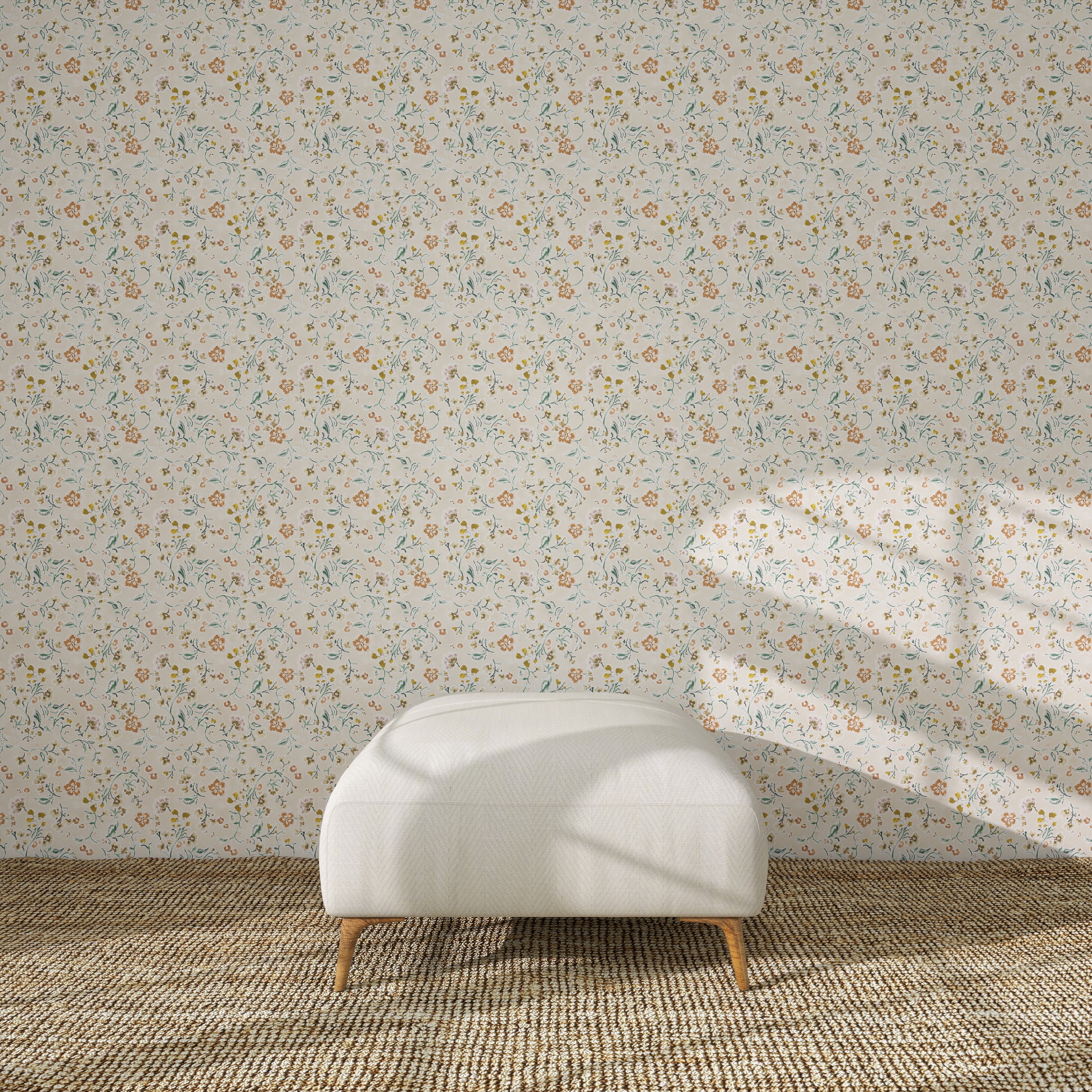 A white upholstered ottoman stands on a beige rug in front of Terra Bloom Wallpaper Sample. Sunlight casts shadows over the ottoman and accentuates the colour and floral design of the wallpaper.