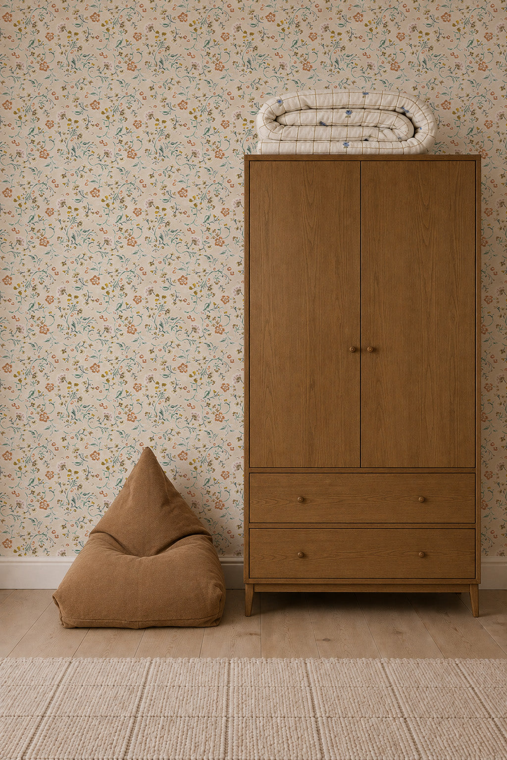 A wooden wardrobe stands against Terra Bloom Wallpaper, with a folded quilt on top and a brown bean bag chair beside it on a light wooden floor.