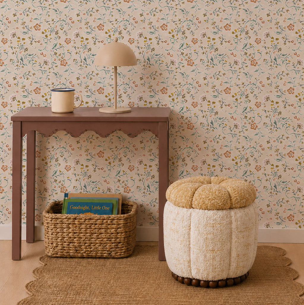 A small brown table with a lamp and container stands against Terra Bloom Wallpaper, adding artistic charm to this nature-inspired nursery. A woven basket with children’s books sits below, next to a round textured stool on a scalloped rug, completing the thoughtful nursery wall decor.