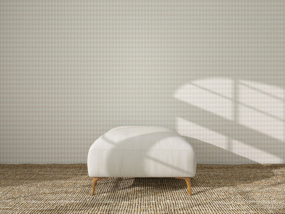 A white ottoman rests on a woven rug before a wall adorned with Diamond Dancer Wallpaper in Cream, as sunlight casts window-shaped shadows across the wall and floor.