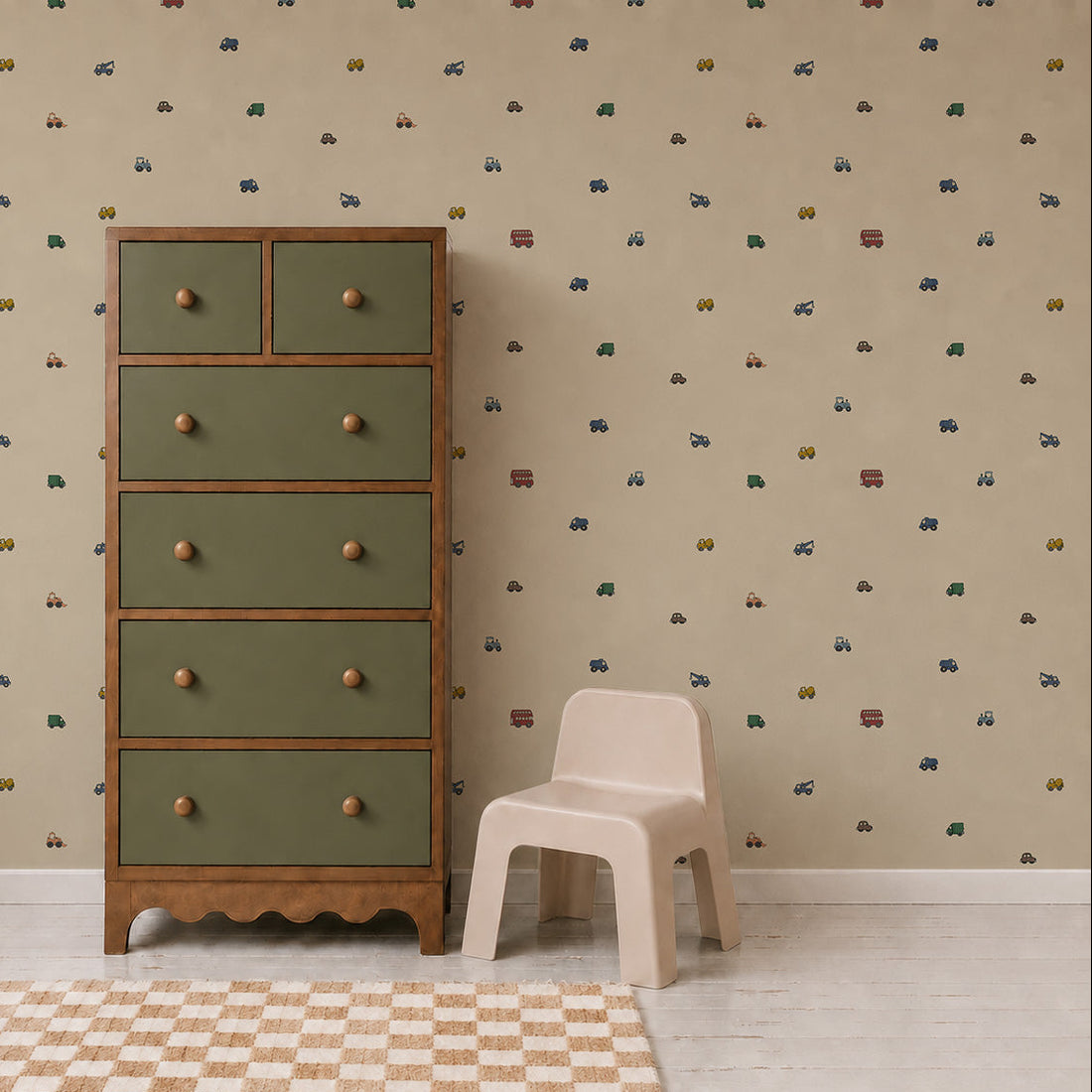A green and wood dresser stands beside a small beige chair on a white floor with a checked rug. The wall features the Transport Trail Wallpaper in Beige, adorned with small colorful vehicles, creating a playful and inviting atmosphere in this charming kids’ room or nursery.