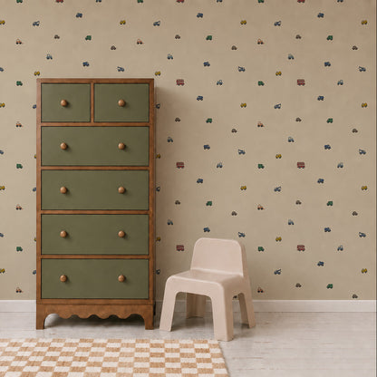 A green and wood dresser stands beside a small beige chair on a white floor with a checked rug. The wall features the Transport Trail Wallpaper in Beige, adorned with small colorful vehicles, creating a playful and inviting atmosphere in this charming kids’ room or nursery.