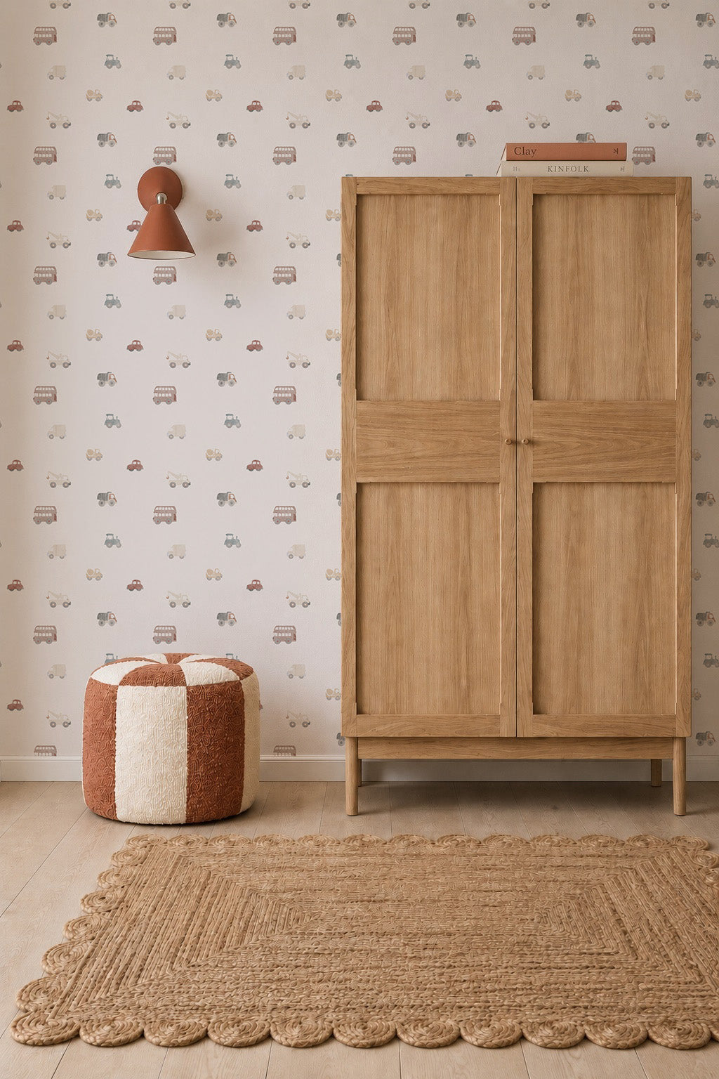 A cozy, neutral-toned nursery featuring a wooden wardrobe, textured rug, red-and-white pouf, brown wall lamp, and Transport Wallpaper adorned with colorful cars.