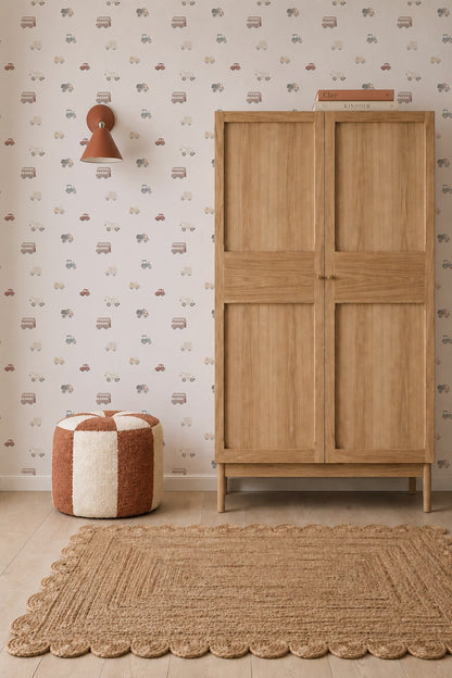 A cozy, neutral-toned nursery featuring a wooden wardrobe, textured rug, red-and-white pouf, brown wall lamp, and Transport Wallpaper adorned with colorful cars.