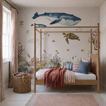 A cozy bedroom featuring a wooden canopy bed, pink and blue bedding, a wicker basket, and the Under The Sea Mural, Watercolour—an enchanting wallpaper showcasing sea creatures such as whales, turtles, fish, and coral. Sunlight filters through sheer pink curtains at the window, creating an inviting retreat perfect for ocean lovers.