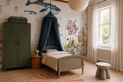 A cozy children’s bedroom designed especially for ocean lovers, featuring the vibrant Under The Sea Mural, Watercolour with playful sea creatures, a canopy bed, green wardrobe, round table, stool, and a window with sheer curtains letting in natural light.
