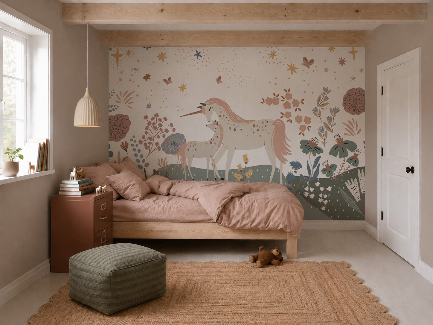 A cozy bedroom features a wooden bed, pink bedding, a jute rug, and the Unicorn Meadow Mural depicting two unicorns in a whimsical floral landscape. A green pouf, teddy bear, and natural light complete the inviting atmosphere.
