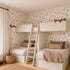 Children’s bedroom featuring two white bunk beds with pastel bedding, a wooden ladder, the Unicorn Party Wallpaper, a wicker basket, and a window with cream curtains for a cozy, whimsical vibe.