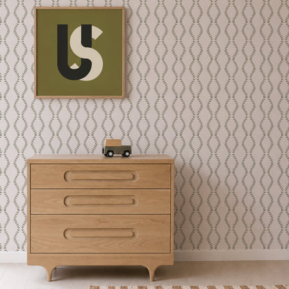 A light wooden dresser with three drawers stands against Vintage Vines Wallpaper, which features delicate, hand-drawn details. On top of the dresser sits a small toy truck. Above, a green and beige abstract art piece is framed and displayed on the wall.