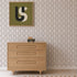 A light wooden dresser with three drawers stands against Vintage Vines Wallpaper, which features delicate, hand-drawn details. On top of the dresser sits a small toy truck. Above, a green and beige abstract art piece is framed and displayed on the wall.