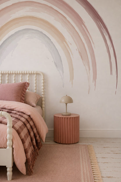 A cozy bedroom features a cream spindle bed with pink bedding, a striped blanket, round pink nightstand with beige lamp, pink rug, and the Iris Watercolour Rainbow Mural—perfect for creating a dreamy girls&
