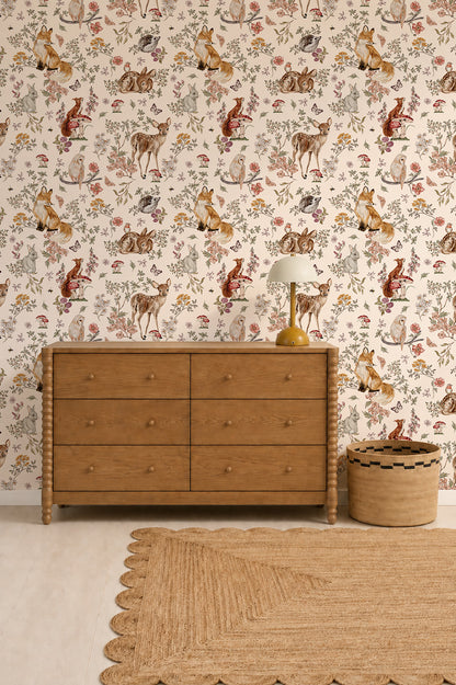 A wooden dresser stands against a wall decorated with Whimsical Woodland Wallpaper, featuring charming forest creatures. A lamp and basket are on and beside the dresser, while a woven rug with scalloped edges softens the light floor.