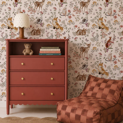 A children’s room with a terracotta dresser, books, a teddy bear, a lamp, a checker-patterned bean bag chair, a round jute rug, a plush bunny toy, and enchanting Whimsical Woodland Wallpaper that brings the magic of nature indoors.