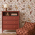 A children’s room with a terracotta dresser, books, a teddy bear, a lamp, a checker-patterned bean bag chair, a round jute rug, a plush bunny toy, and enchanting Whimsical Woodland Wallpaper that brings the magic of nature indoors.