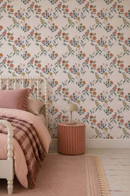 A cozy bedroom with Wildflower Posy Wallpaper featuring delicate floral patterns, pale pink bedding, a round pink nightstand with a small lamp, and a matching rug on a light wooden floor.