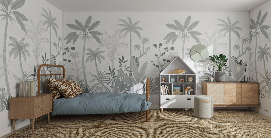 A cozy, modern bedroom features Natural Wonder Palm Wallpaper Mural Slate, a rattan rug, single bed with blue bedding, wooden furniture, bookshelves, potted plants, and a large window filling the space with natural light.