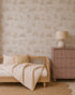 Minimalist bedroom with a light wooden bed, striped bedding, round woven rug, mauve dresser with lamp, and Woodland Wonder Wallpaper, Neutral—featuring a subtle animal pattern. The soft, neutral color palette creates a calm atmosphere.