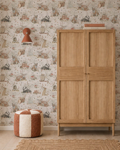 A cozy room featuring Woodland Wonder Wallpaper, a wooden wardrobe, a round brown-and-white pouf, a woven rug, and a wall sconce with a reddish shade.